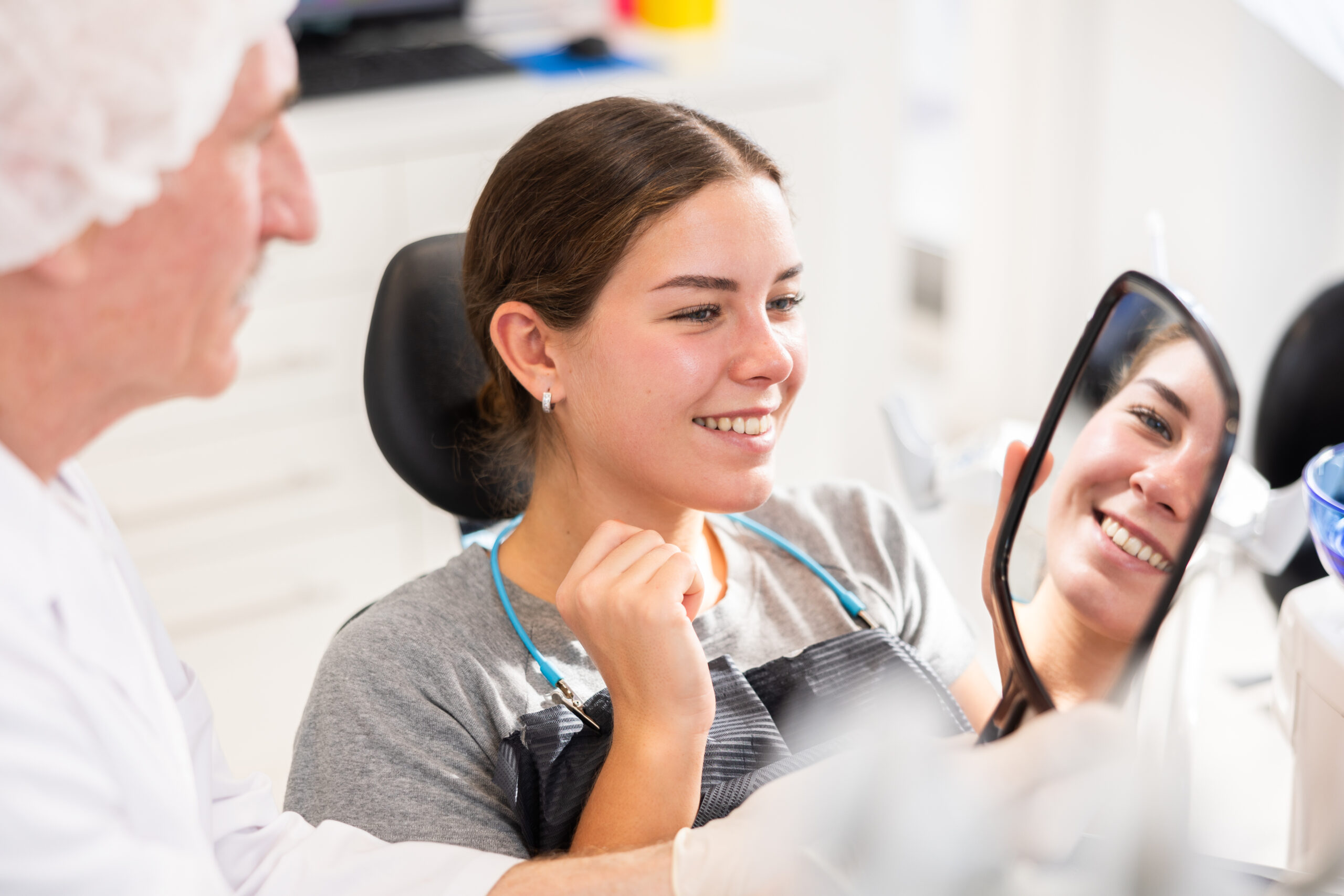 Elderly male dentist showing young female patient result of dental procedure in dental clinic