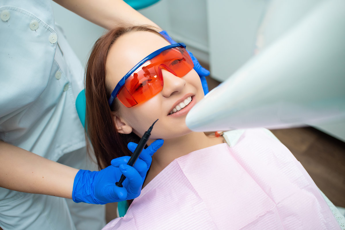 Beautiful girl with red hair is sitting in the dental chair. Treatment and prevention of dental diseases. Teeth whitening